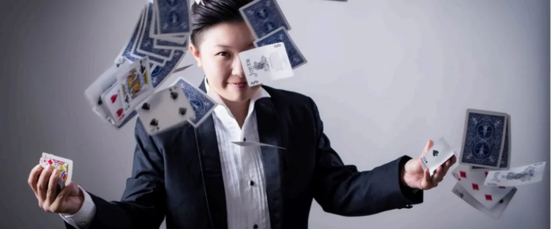 A person in a suit joyfully juggles playing cards in mid-air against a neutral background. The scene conveys a sense of magic and skillful performance.