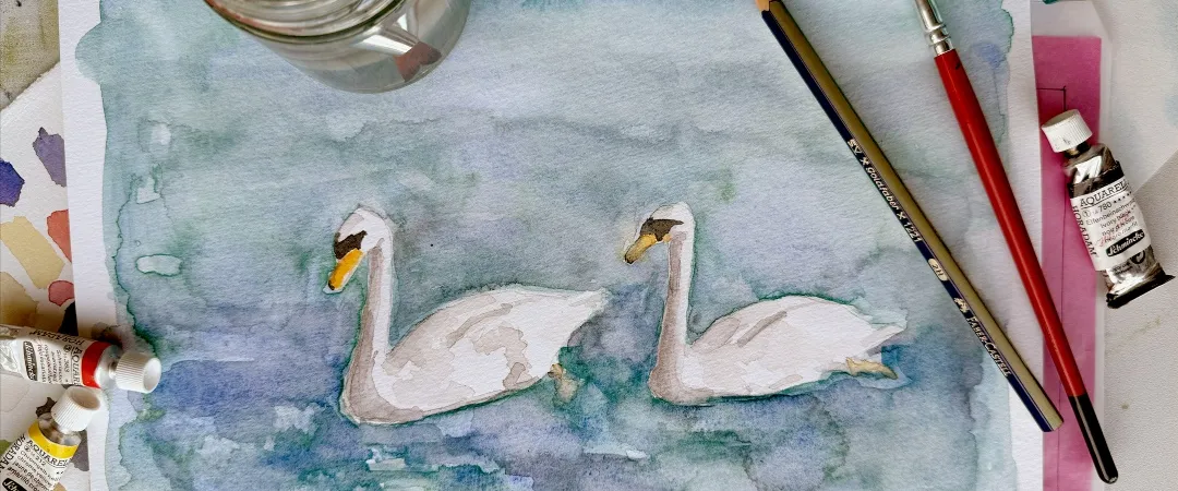 A watercolor painting depicts two swans on calm water. Surrounding are paintbrushes, pencils, and colourful paint tubes, evoking a serene artistic mood.