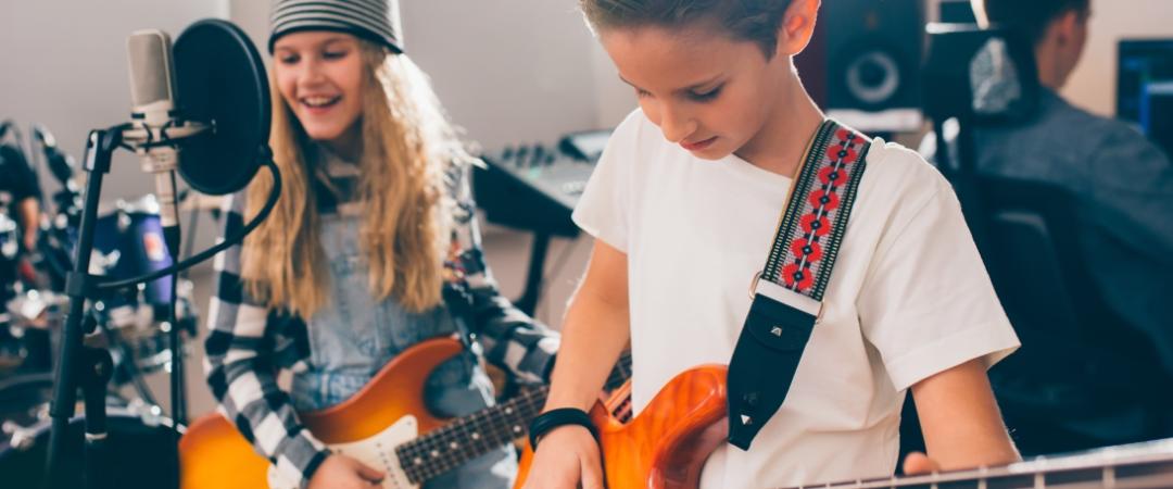 Girl and boy holding guitars standing behind microphones