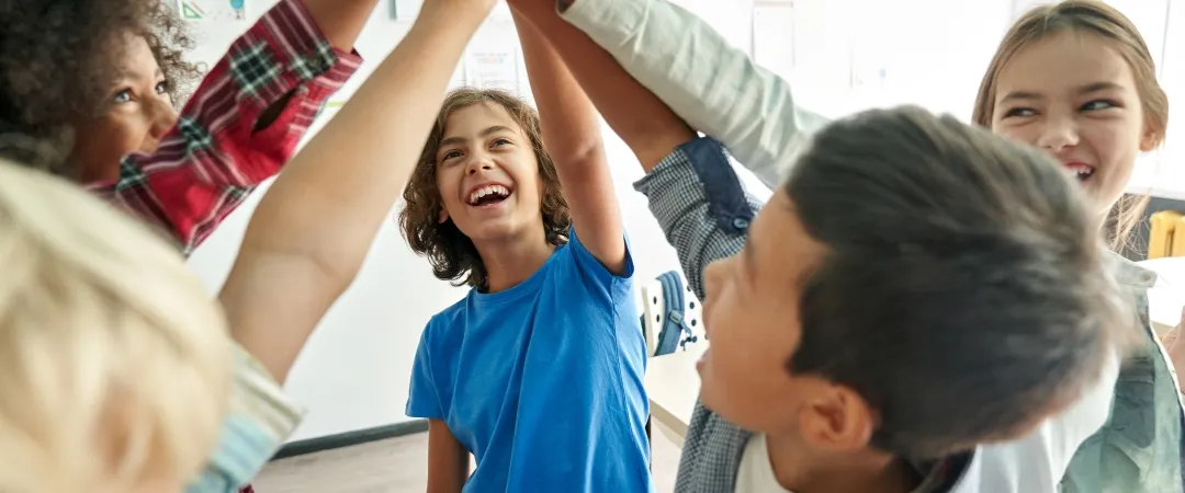 Happy diverse multiethnic kids junior school students group giving high five together in classroom. Excited children celebrating achievements, teamwork, diversity and friendship with high five 