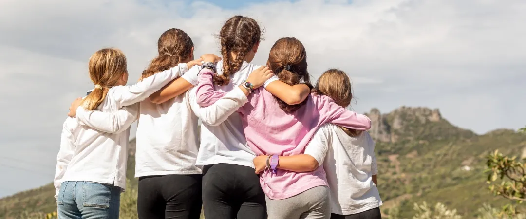 Five girls with their arms around each other looking towards a mountain