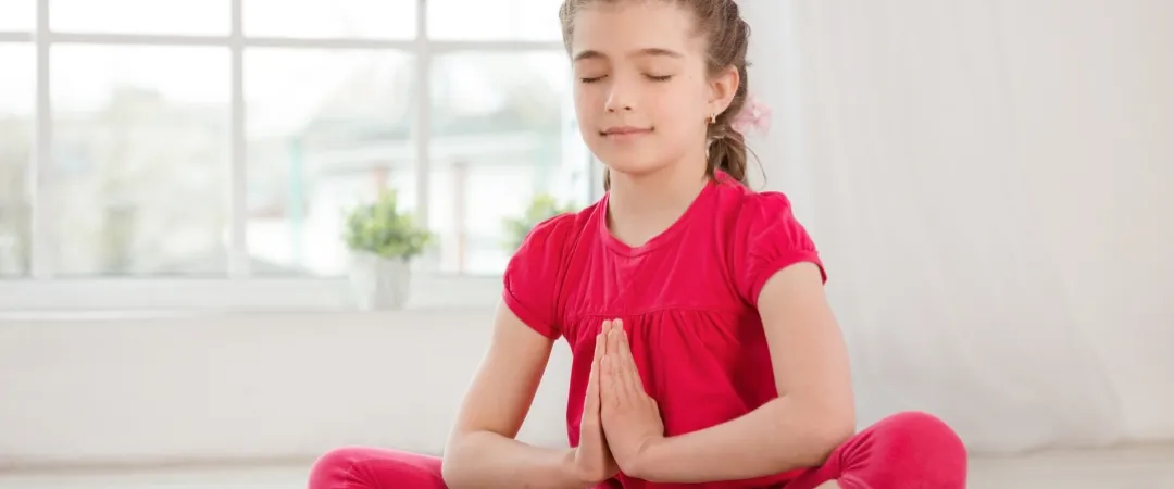 Child in red clothes meditates on floor with hands together