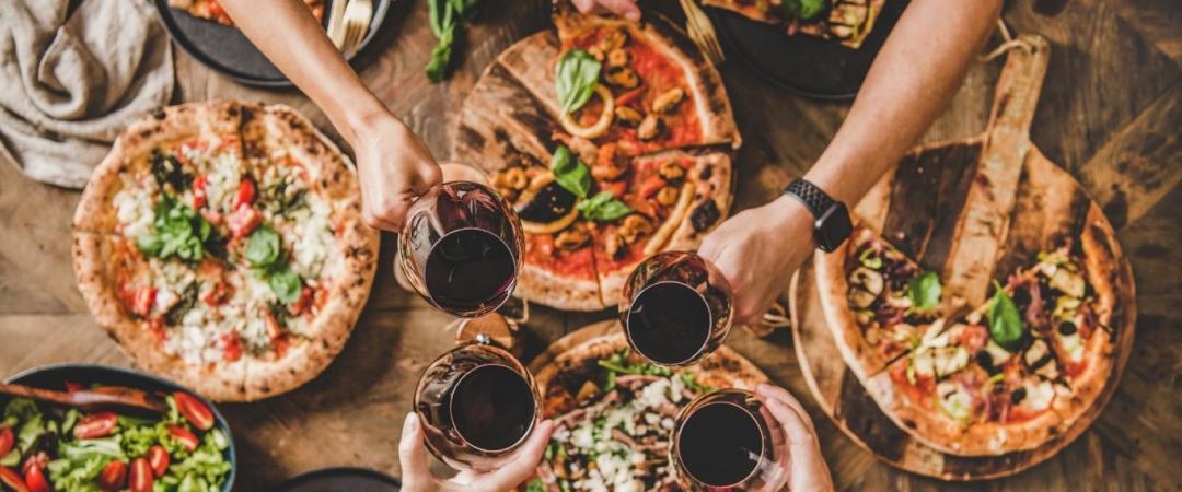 people sharing pizza and cheersing with wine
