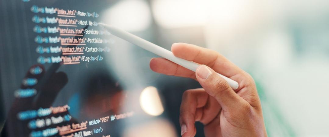 A person’s hand uses a stylus to interact with a screen displaying HTML code