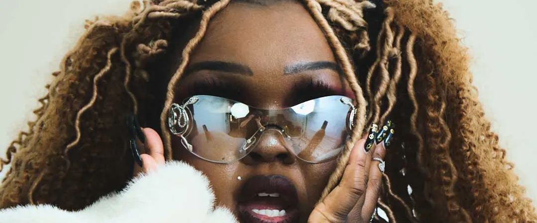 A woman with blonde braids and bold makeup, wearing sunglasses and a white fur coat.