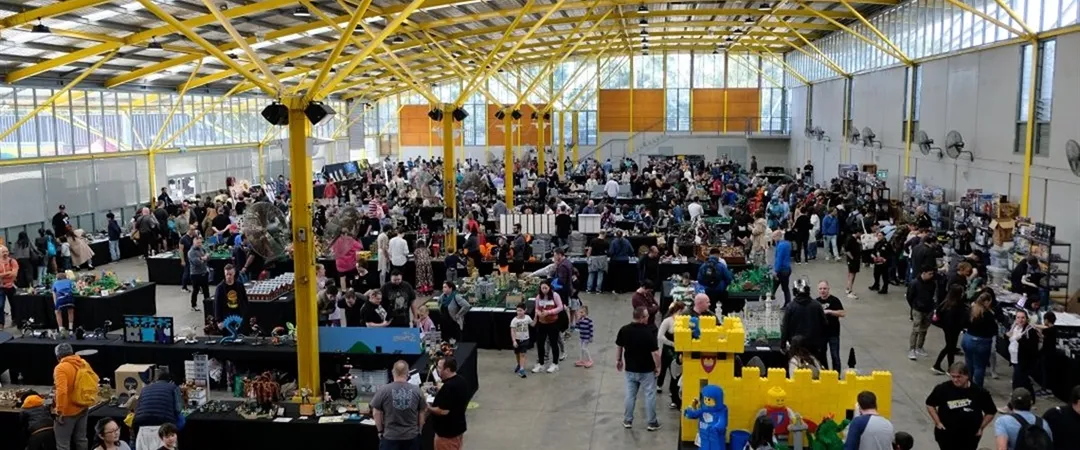A bustling indoor expo with people browsing vendor stalls under a large yellow-roofed space, conveying a lively and engaging atmosphere.