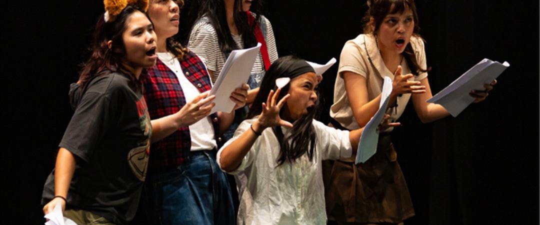 Five people on stage wear animal ear headbands and casual clothes, playfully posing with animated expressions. The scene is lively and theatrical.
