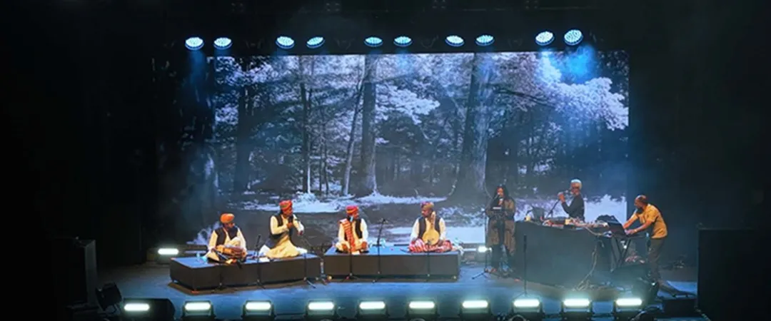 Silhouetted crowd faces a stage with musicians and large screens showing vibrant digital portraits of women with futuristic, mechanical features. Energetic ambiance.