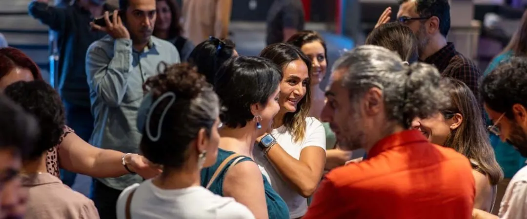 Diverse group of people mingle and chat at a lively indoor gathering, smiling and engaged in warm, social conversation.