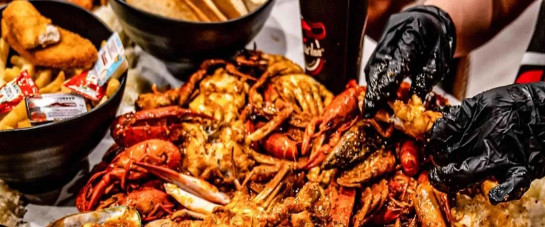 A seafood boil feast with crabs, crawfish, and shrimp, served on a table with hands wearing black gloves picking at the seasoned shellfish pieces.