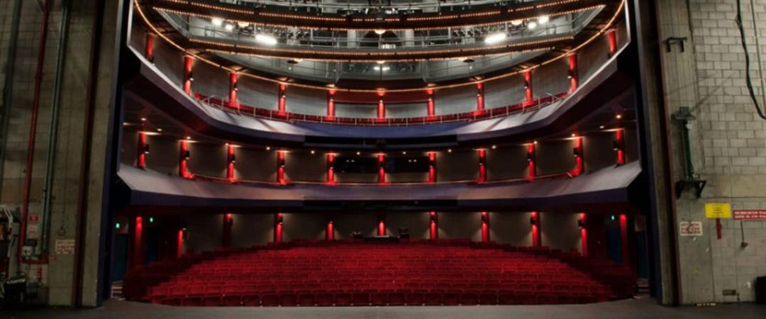 View from a stage into a grand theater with red seats and ornate balconies. The open space conveys anticipation and elegance.
