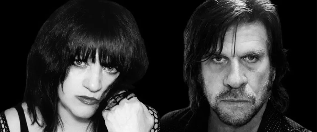 Black and white photo of a woman and a man with intense expressions against a dark background.