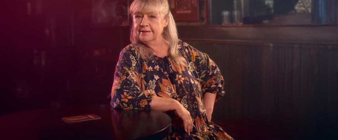 A woman sitting at a table in a bar, casually enjoying her drink and engaging in conversation.