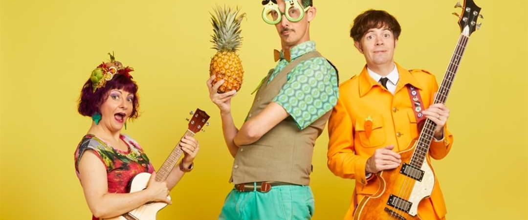 Three people dressed in colorful attire stand together, each holding a guitar and a pineapple, exuding a cheerful vibe.