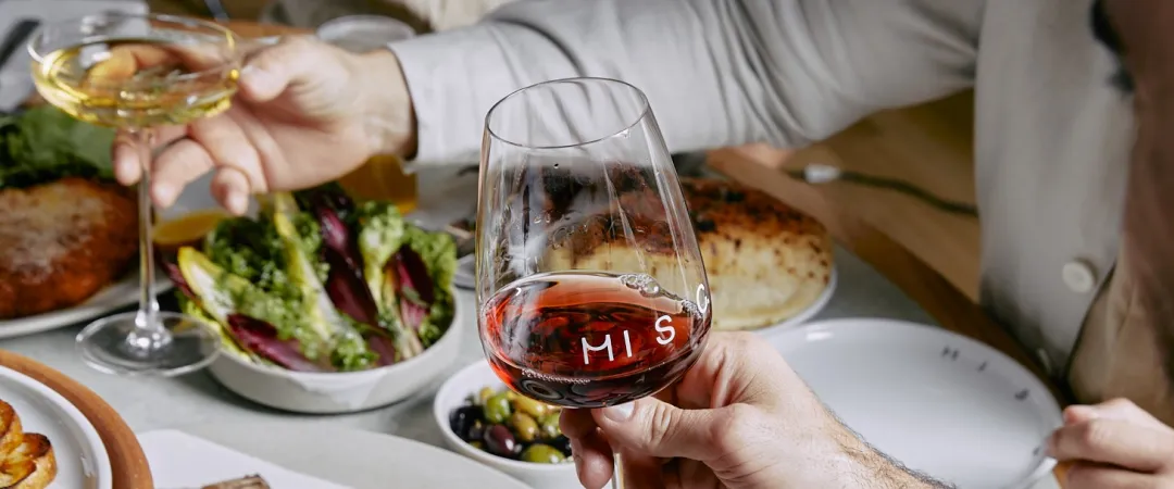 Friends toast with red and white wine at a restaurant table, surrounded by steak, salad, fries, and shared plates in a warm, festive setting.