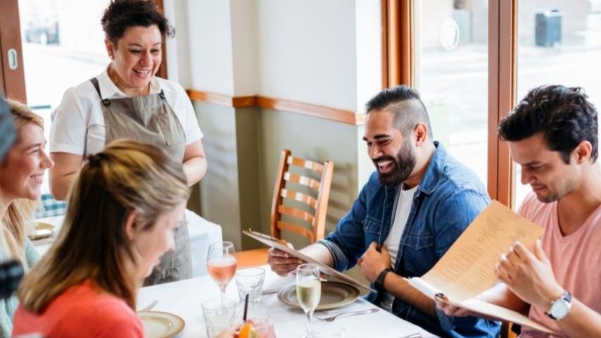 people at a restaurant laughing with a waitress taking their orders