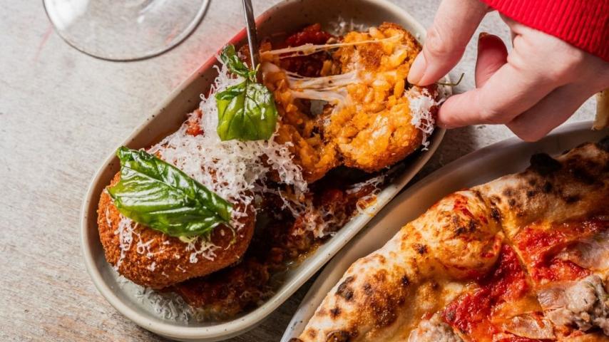 Hand pulling cheese arancini from a rectangle plate