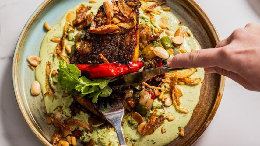 Knife cutting into crispy skin salmon sitting on green sauce