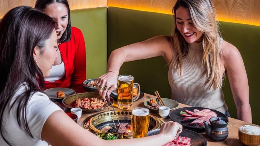 People cooking meat on the BBQ and drinking beer from large glasses 