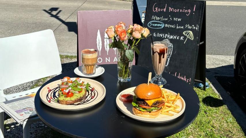 Small round table sitting on grass with 2 plates of food: avocado and pancakes