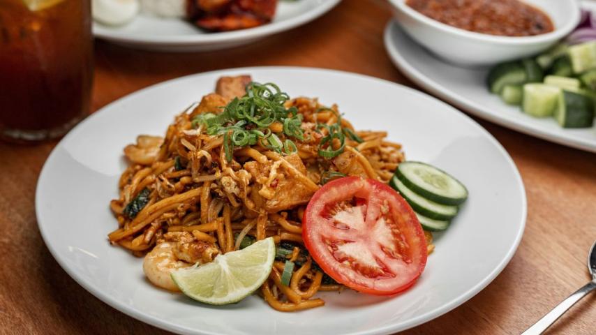 Plate of noodles and meat with a topping of tomatoes and cucumber