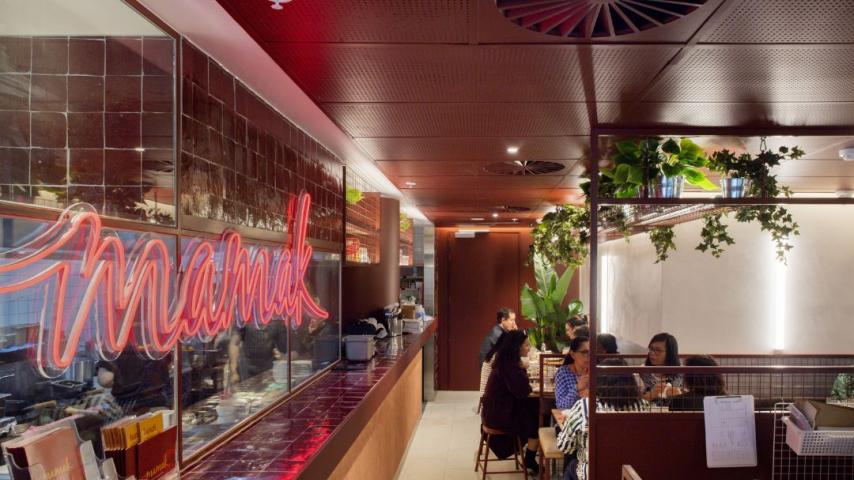 Read neon writing of 'mamak' looking into a restaurant area with people sitting at tables 