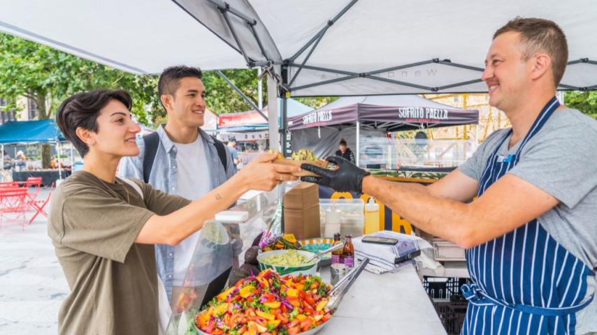 Man in blue apron smiling and handing over fruit food for a man in green