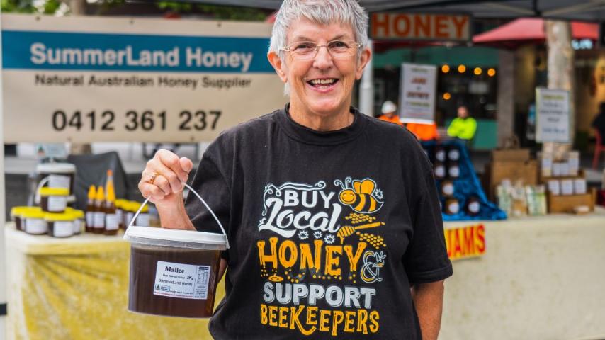 Women with grey hair smiling and holding a bucket of honey